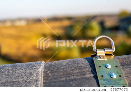 Selective focus on a metal temporary anchor installed on the peak of a roof for fall protection. Selective focus on a metal temporary anchor installed on the peak of a roof for fall protection. 97677073