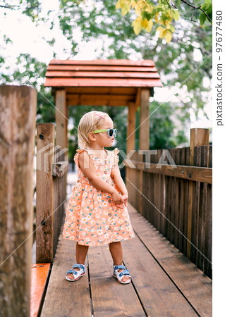 Little girl in sunglasses stands with her head turned on a wooden bridge. High quality photo Little girl in sunglasses stands with her head turned on a wooden bridge. High quality photo 97677480