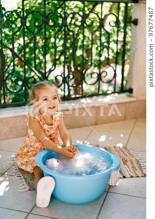 Smiling little girl washes a toy in a bowl on the balcony. High quality photo Smiling little girl washes a toy in a bowl on the balcony. High quality photo 97677487