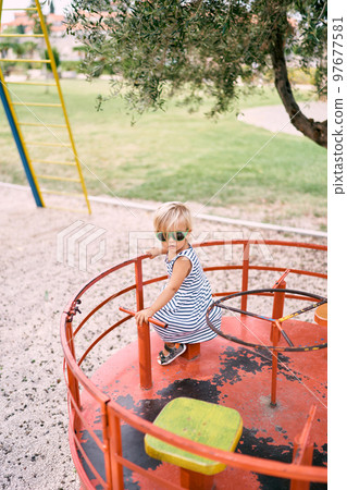 Little girl in sunglasses rides a spinning carousel on the playground. High quality photo 97677581
