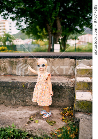 Little girl stands near a high stone curb and points to it with her hand. High quality photo Little girl stands near a high stone curb and points to it with her hand. High quality photo 97677688