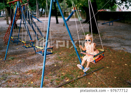 Little girl in sunglasses swings on a rope swing at the playground. High quality photo 97677712