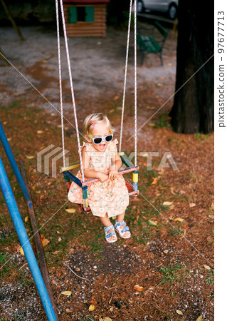 Little girl sits with her mouth open on a swing in the playground. High quality photo Little girl sits with her mouth open on a swing in the playground. High quality photo 97677713