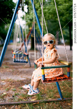 Little girl sits with her head turned on a swing in the playground. High quality photo Little girl sits with her head turned on a swing in the playground. High quality photo 97677714