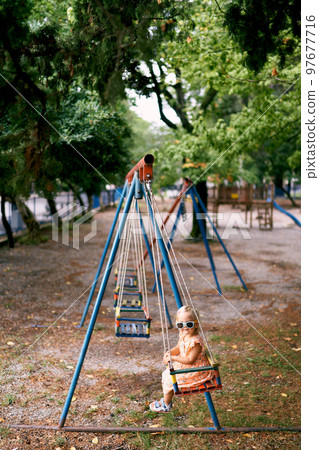 Little girl sitting with her tongue hanging out on a swing. High quality photo Little girl sitting with her tongue hanging out on a swing. High quality photo 97677716