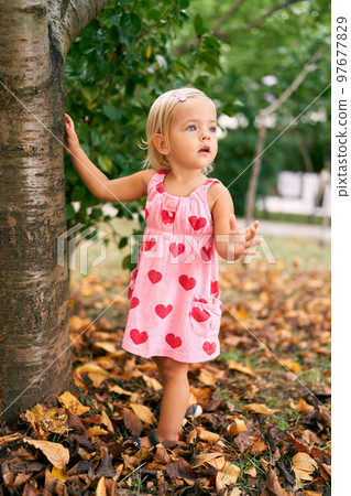 Little girl stands leaning on a tree with her hand in the garden. High quality photo Little girl stands leaning on a tree with her hand in the garden. High quality photo 97677829