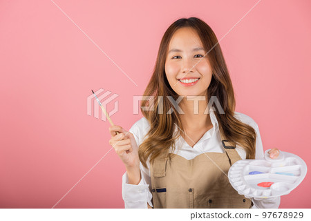 Portrait Asian young woman artist holding brush and paint palette, Happy female painting using paintbrush and palette with colors, studio shot isolated on pink background, Art design workshop 97678929
