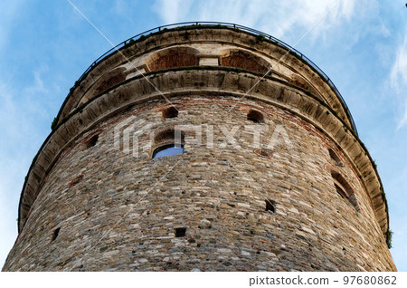 View of Galata Tower from below surrounded by classic buildings against blue sky 97680862