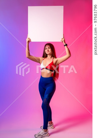 Confident young sportswoman showing empty banner in bright studio Confident young sportswoman showing empty banner in bright studio 97683796