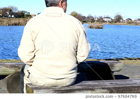 An old man relaxing in the sun on a park bench with the winter sun on his back An old man relaxing in the sun on a park bench with the winter sun on his back 97684769