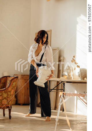 a brunette in a white shirt and trousers with suspenders in the artist's studio. a brunette in a white shirt and trousers with suspenders in the artist's studio. 97685067