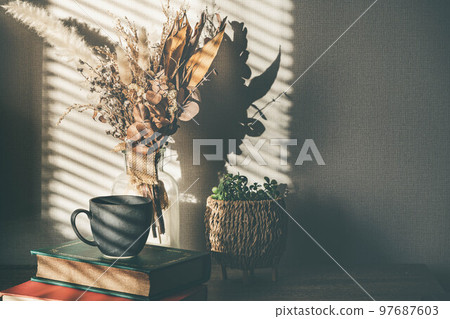 Light by the window, dried flowers, books and cups 97687603