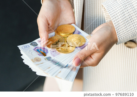 Young business woman holding British pounds and bitcoin in hands, close up of female hands with cash equivalents. 97689110