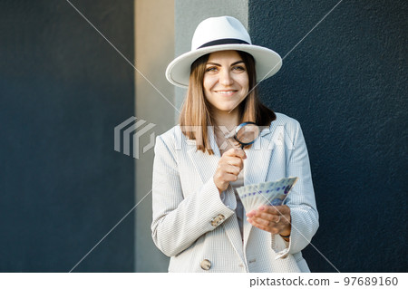 Attractive woman with cash in her hands and magnifying glass. Woman examines banknotes in her hands Attractive woman with cash in her hands and magnifying glass. Woman examines banknotes in her hands 97689160