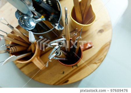 Various tools for carving pottery in mug placed on wooden table in workshop with professional instruments, top view Various tools for carving pottery in mug placed on wooden table in workshop with professional instruments, top view 97689476