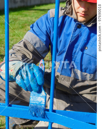 Professional painter in clothing and helmet paints metal fence or fence made of reinforcement with Professional painter in clothing and helmet paints metal fence or fence made of reinforcement with 97690018