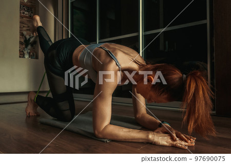 Muscular and athletic woman trains at home in room. Fitness at home. Woman kneels and performs Muscular and athletic woman trains at home in room. Fitness at home. Woman kneels and performs 97690075