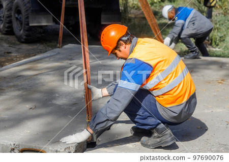 Slinger lays concrete slab on construction site on summer day. Worker in protective vest and Slinger lays concrete slab on construction site on summer day. Worker in protective vest and 97690076
