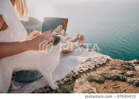 Woman sea laptop. Business woman petting cat and working on laptop by the sea. Close up on hands of pretty lady typing on computer outdoors summer day. Freelance, digital nomad and holidays concept. 97690410