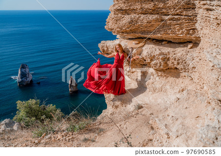 A woman in a red flying dress fluttering in the wind, against the backdrop of the sea. 97690585