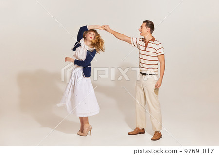 Excited young, beautiful, stylish couple in vintage style fashion clothes dancing isolated over light background. 60s, 70s american culture concept Excited young, beautiful, stylish couple in vintage style fashion clothes dancing isolated over light background. 60s, 70s american culture concept 97691017