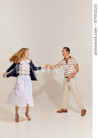 Excited young, beautiful, stylish couple in vintage style fashion clothes dancing isolated over light background. 60s, 70s american culture concept 97691020
