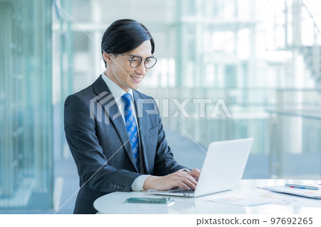 Portrait of smiling businessman sitting in front of laptop at desk Portrait of smiling businessman sitting in front of laptop at desk 97692265