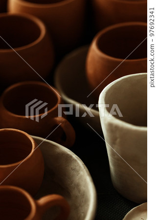 A close-up of various drying clay tableware on a shelf. A pottery studio concept. Craftmade dishes, bowls, pots, mugs of different colors. Cozy view. workshop with ceramic dishware A close-up of various drying clay tableware on a shelf. A pottery studio concept. Craftmade dishes, bowls, pots, mugs of different colors. Cozy view. workshop with ceramic dishware 97692341