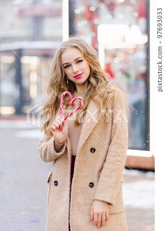 A happy smiling lady poses at a street holiday fair, holding lollipops in her hands. A funny girl makes a heart out of lollipops on a stick. The concept of Christmas or Valentine's Day A happy smiling lady poses at a street holiday fair, holding lollipops in her hands. A funny girl makes a heart out of lollipops on a stick. The concept of Christmas or Valentine's Day 97693033