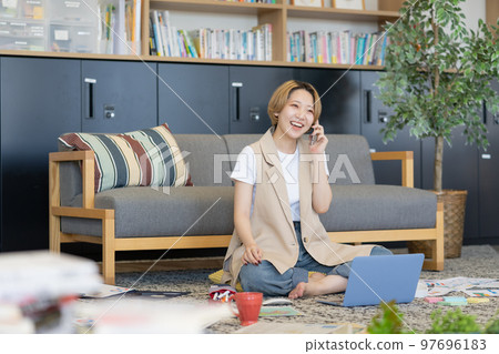 一名年輕女子在地板上散佈文件，並在她的智能手機上交談 97696183