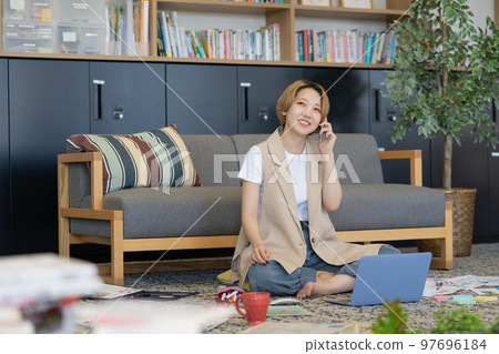 一名年輕女子在地板上散佈文件，並在她的智能手機上交談 97696184