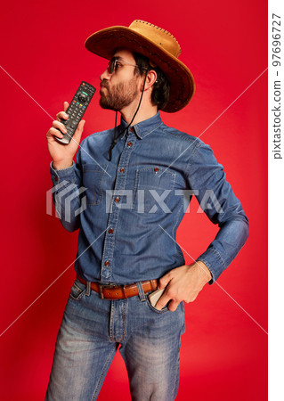 Excited young man in cowboy style outfit having fun, posing isolated over red background. Model in cowboy hat and denim clothes. Fashion, emotions concept Excited young man in cowboy style outfit having fun, posing isolated over red background. Model in cowboy hat and denim clothes. Fashion, emotions concept 97696727
