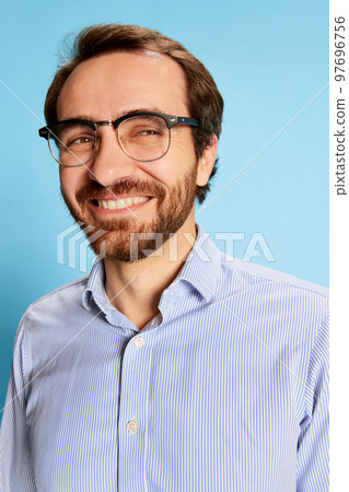 Sincerely smile. Portrait of mature bearded man in eyewear expressing happy emotions on his face isolated over blue background. Business, mental health, emotions concept Sincerely smile. Portrait of mature bearded man in eyewear expressing happy emotions on his face isolated over blue background. Business, mental health, emotions concept 97696756