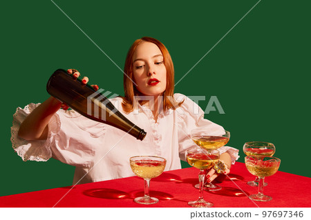 Young redhead girl in festive white dress sitting at the table with champagne over green background. Degustation Young redhead girl in festive white dress sitting at the table with champagne over green background. Degustation 97697346