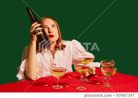 Young redhead girl in festive white dress sitting at the table with champagne over green background. Hangover Young redhead girl in festive white dress sitting at the table with champagne over green background. Hangover 97697347