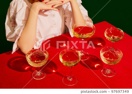 Cropped image of woman in white dress sitting at the table with champagne glasses on red tablecloth over green background Cropped image of woman in white dress sitting at the table with champagne glasses on red tablecloth over green background 97697349