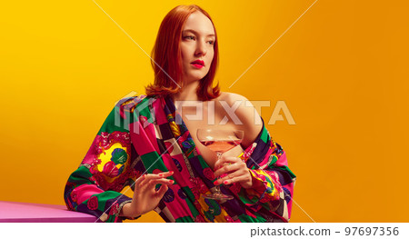 Young beautiful woman in bright costume holding champagne over yellow background. Female party. Traditional taste Young beautiful woman in bright costume holding champagne over yellow background. Female party. Traditional taste 97697356