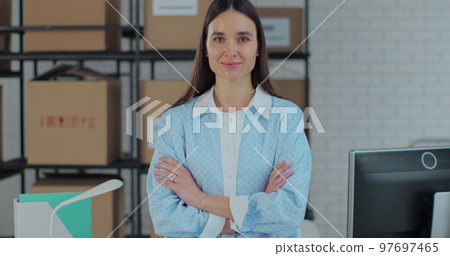 Portrait of an attractive woman looking at the camera, crossing her arms. The owner of a successful business works in a warehouse in an online store. Portrait of an attractive woman looking at the camera, crossing her arms. The owner of a successful business works in a warehouse in an online store. 97697465