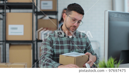 Man business owner checking stock on computer in a warehouse full of shelves with goods. Work in the distribution center with a colleague. Man business owner checking stock on computer in a warehouse full of shelves with goods. Work in the distribution center with a colleague. 97697475