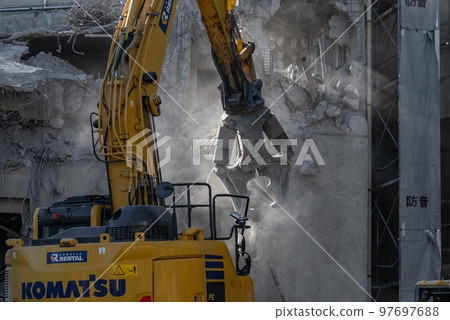Building demolition: sunlight, dust and a large splitting machine 97697688