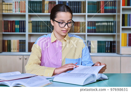 Teenage girl student looking at book, studying in library 97698631