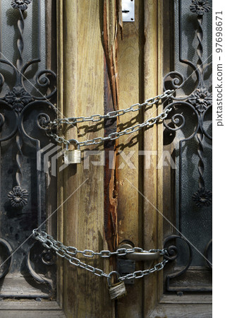 Old wooden door of an abandoned house is locked. Chain on the vintage door of a closed mansion 97698671
