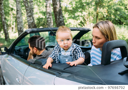 Mom, dad and little son in a convertible car. Summer family road trip to nature 97698702