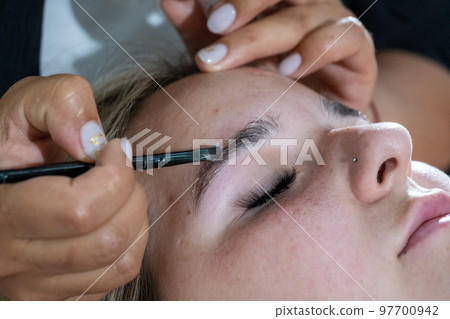 Makeup artist laminates woman eyebrows before tinting Makeup artist laminates woman eyebrows before tinting 97700942