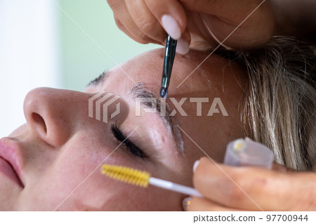 Hands of makeup artist apply means for laminating eyebrows Hands of makeup artist apply means for laminating eyebrows 97700944