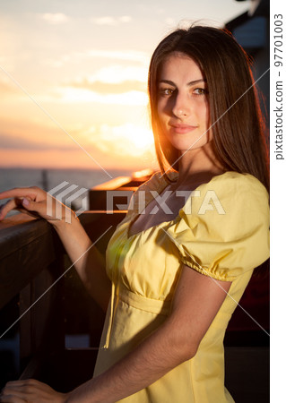 Young woman sits sideways holding on railing of balcony Young woman sits sideways holding on railing of balcony 97701003