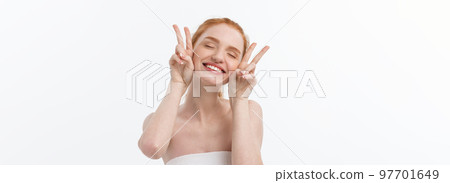 Close-up of beautiful young woman with bath towel covering her breasts, on gray, shows two fingers sign. Close-up of beautiful young woman with bath towel covering her breasts, on gray, shows two fingers sign. 97701649