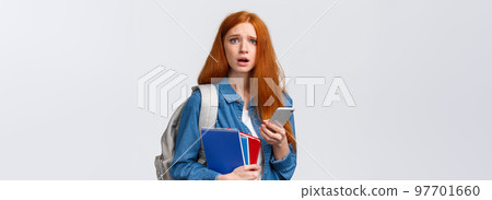 Uneasy and sad gloomy cute redhead female looking troubled camera, reading something worrying on smartphone display, holding mobile, backpack and notebooks as in university Uneasy and sad gloomy cute redhead female looking troubled camera, reading something worrying on smartphone display, holding mobile, backpack and notebooks as in university 97701660