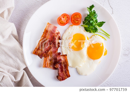 Fried eggs and bacon, tomatoes and parsley on a plate. Homemade breakfast. Top view. Closeup 97701739