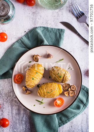 Baked hasselback potatoes with garlic and rosemary on a plate. Homemade lunch. Top and vertical view Baked hasselback potatoes with garlic and rosemary on a plate. Homemade lunch. Top and vertical view 97701756